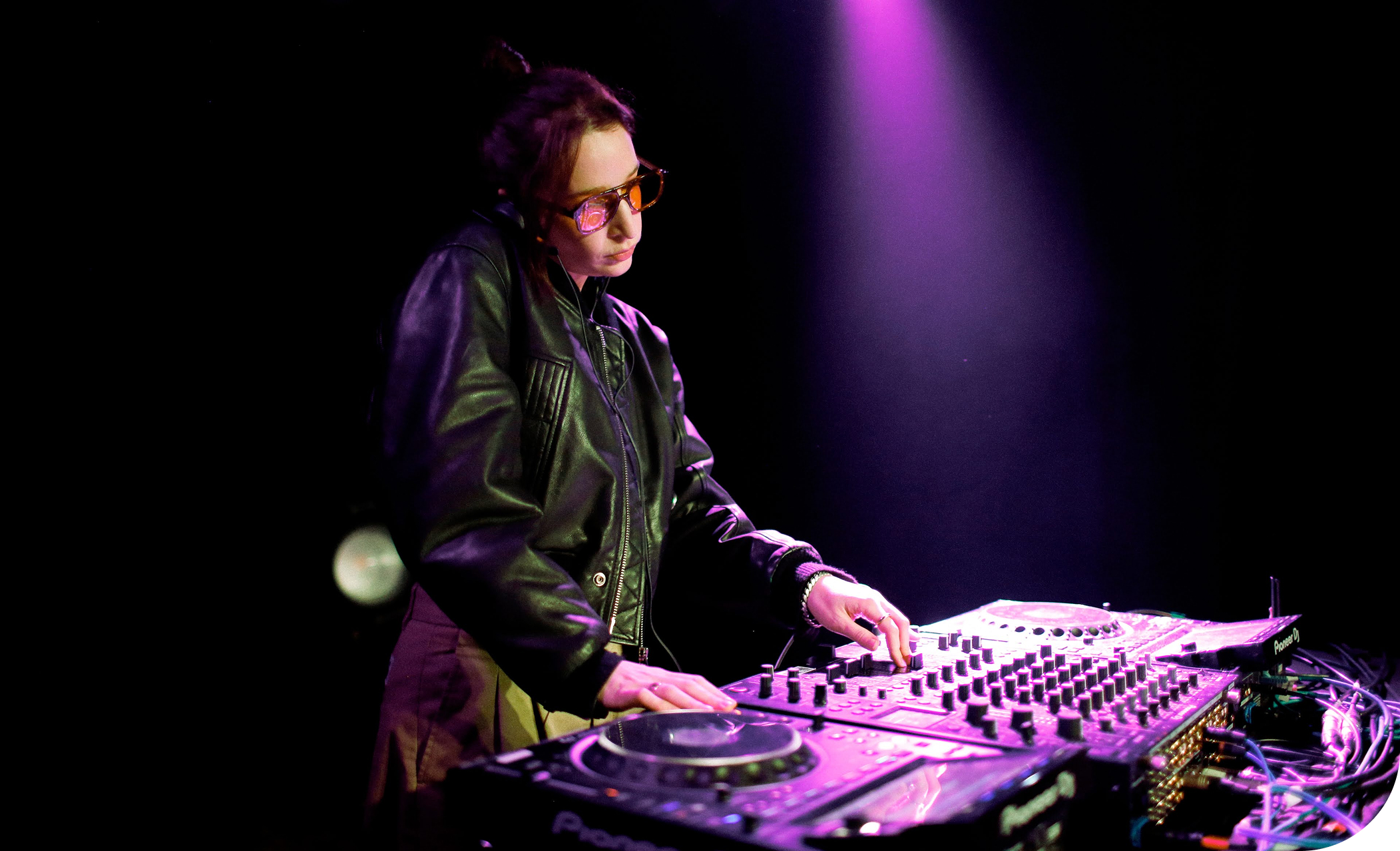 A woman in a black leather shirt mixing music on professional DJ equipment.